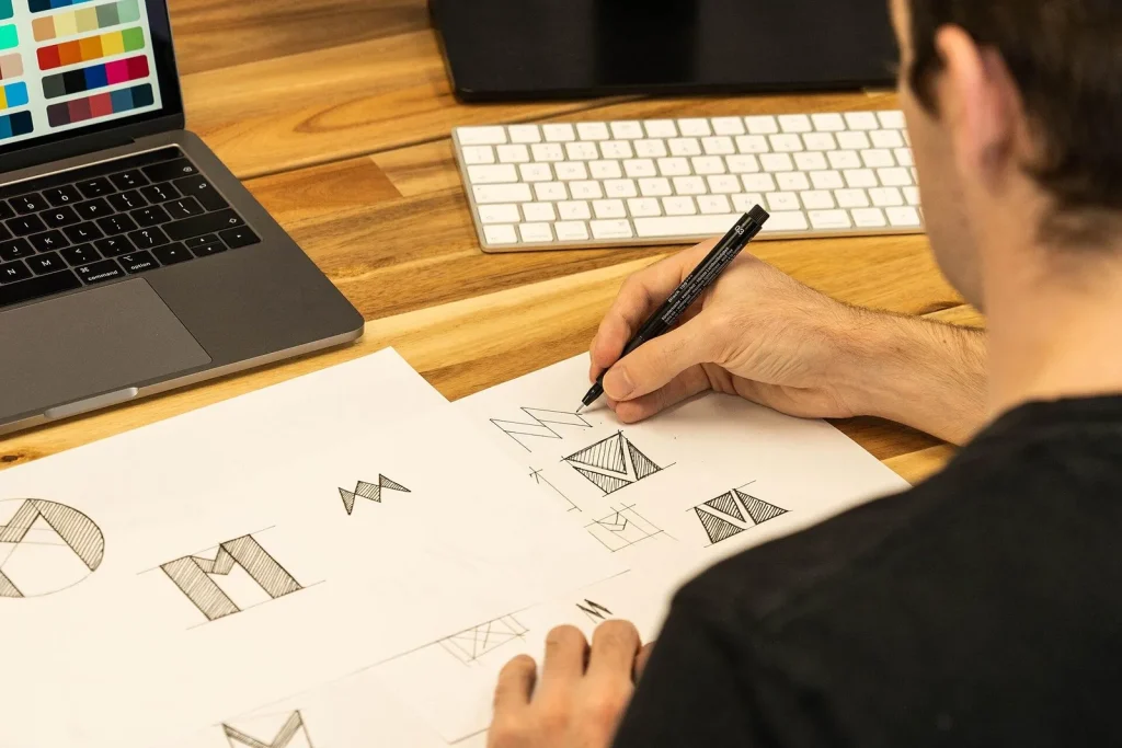 Designer sketching logo concepts on paper beside a laptop — rebranding dubai