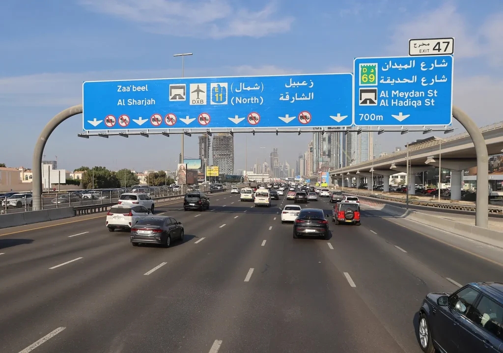 Traffic on a Dubai highway under bilingual road signs — Google Ads vs SEO for Car Rental