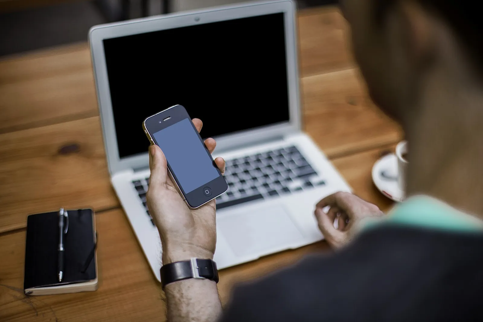 Person checking a smartphone in front of a laptop